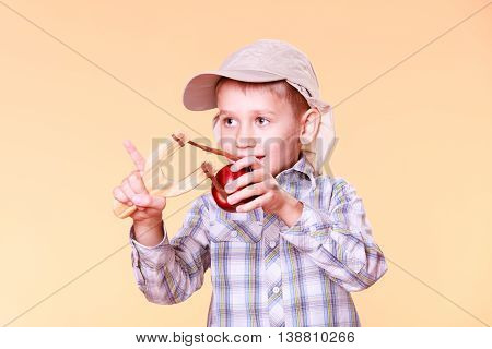 Nature and free time prankster little boy. Child have fun with wooden sling shot and fruit hold apple.