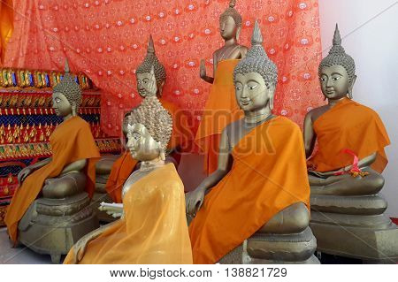 six life size Buddha statues with orange wraps in Buddhist temple near Ranot, Thailand, orange cloth hanging behind them, decorated podium edge seen behind statues