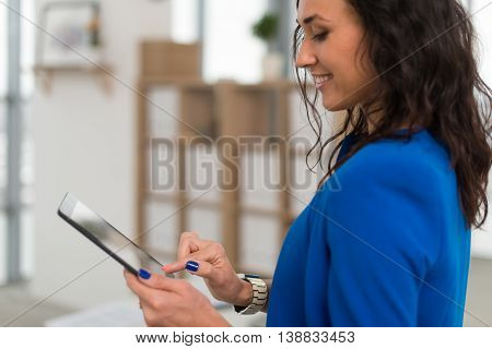 Portrait of an office manager holding her tablet, typing, using wi-fi internet and applications touching the pda screen
