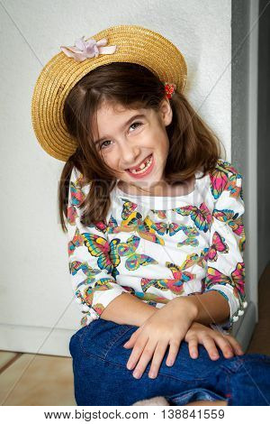 A cute young snaggletooth girl smiles with her while leaning up against a wall with hands crossed at her wrists.