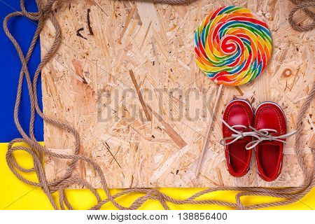 Small Red Boat Shoes Near Big Multi-colored Lollipop  And Rope On Wooden Desk With  Background.  Top