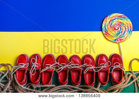 Small Red Boat Shoes Near Big Multi-colored Lollipop On Background. Top View, Copy Space. Frame. Gro
