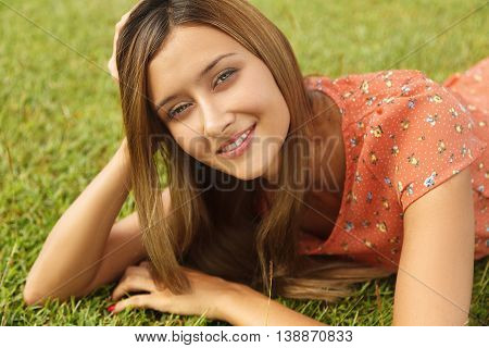 Beautiful girl lying on the grass and smiling while looking at the camera. Horizontal photo