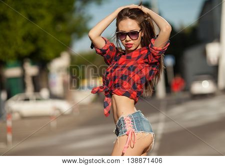 Portrait of the young beautiful smiling woman outdoors enjoying summer sun. Young woman outdoors portrait. Woman in jeans shorts and red shirt. Sexy woman buttocks.