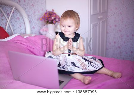 baby in pink room sitting on the bed and playing or watching cartoons price. Girl sitting at home. little princess in dress uses advanced fashion technology