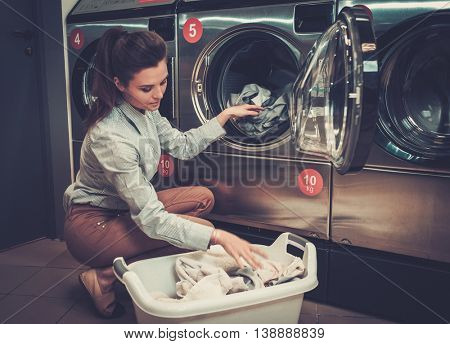 Beautiful woman doing laundry at laundromat shop.