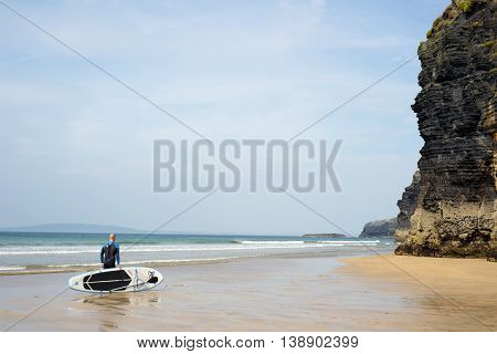 Ballybunion beach, county Kerry, Ireland - September 11, 2014: surfer standing with board on ballybunion beach in the wild atlantic way