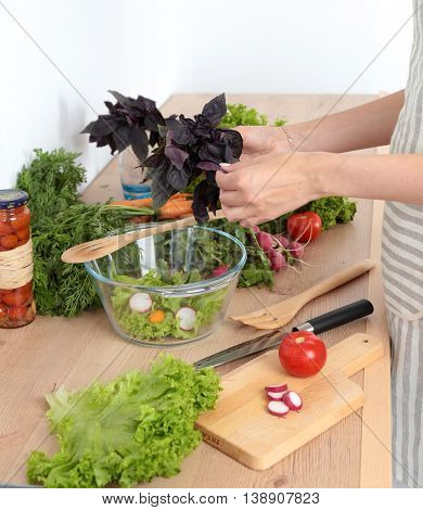 Young woman mixing fresh salad in kitchen