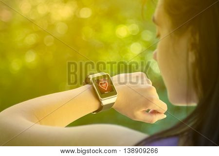Young female athlete looking at heart rate app and checking beats per minute on her smart watch in the park. Fitness, healthy lifestyle and new technology concepts.