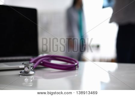 Laptop and stethoscope on the desk doctors standing in the background.