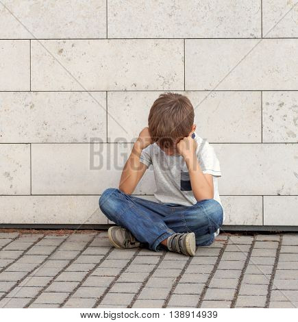 Sad, lonely, unhappy, disappointed, upsed, tired child sitting alone on the ground Outdoor