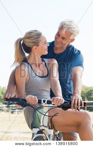 Active senior couple together riding bicycle and looking at each other. Senior smiling couple in the park riding cycle. Senior husband giving cycle ride to mature wife.