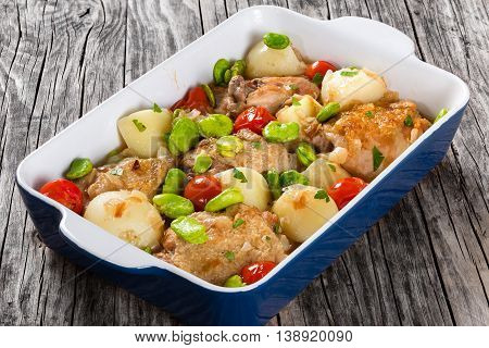 stewed chicken meat new potatoes tomatoes and butter lima bean on graten dish on old wooden table view from above close-up
