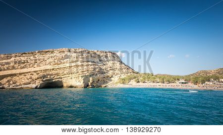 Matala beach on Crete island, Greece. Tourists relax and bath in crystal clear water of Matala in south of Creta. There are many caves near the beach.