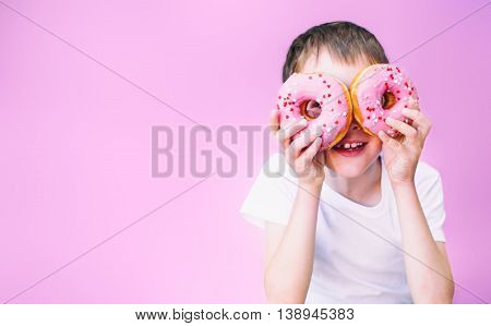 boy looking through pink donuts. child holding a donuts in two eyes like glasses and having fun. pink background. isolated. empty space for your text