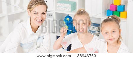 Close shot af a young woman sitting close to two girls with the case full of toys behind them