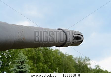 Fragment of tank barrel on background blue sky and green trees. Era of Second World War.