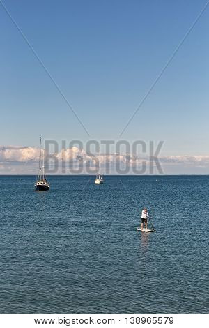 Swanage Dorset UK - July 2016. Eldery male paddles a paddleboard at the sea
