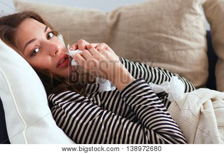 Portrait of a sick woman blowing her nose while sitting on the sofa.