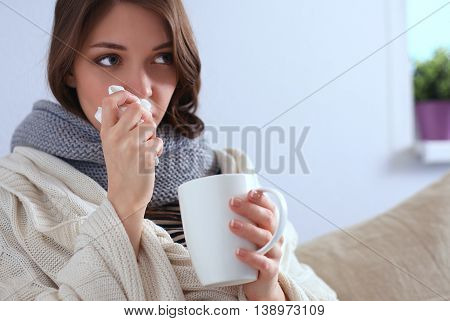 Portrait of a sick woman blowing her nose while sitting on the sofa.