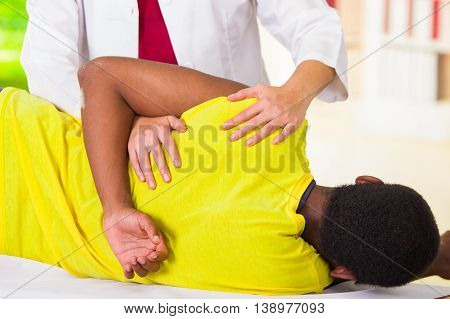 Man lying down getting physical shoulder treatment from physio therapist, patient looking into camera while her hands working on his upper arm area, medical concept.