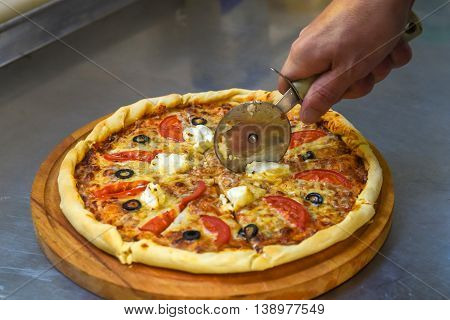 Man cuts a slice of classic homemade Italiancheese pizza just out of the oven