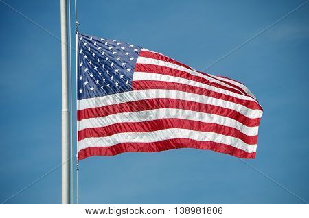 Shiny and silky American flag flying half mast against bright blue sky