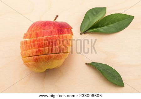 The Sliced Apple That Retained Its Shape Rests On A Wooden Table With Green Flatteries.