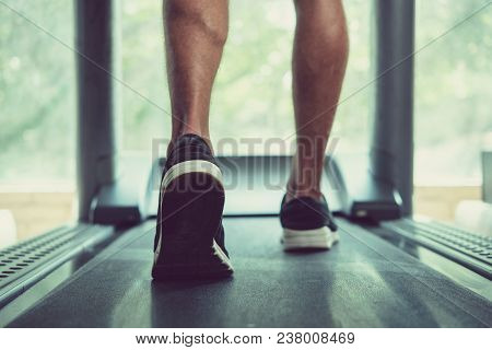 Feet Of Man Walking On Threadmill, View From The Back