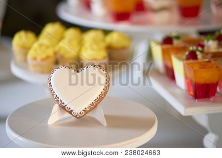 Close-up Of A Sweet Gingerbread Cookie, Covered With White Glaze Stands On The Wooden Stand In Front