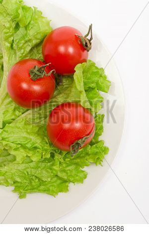 Three Cherry Tomatoes, Lettuce Leaves On A White Plate And White Background
