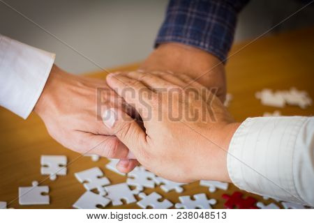 The Hands Of Three Business People Have A Jigsaw Puzzle As A Background.