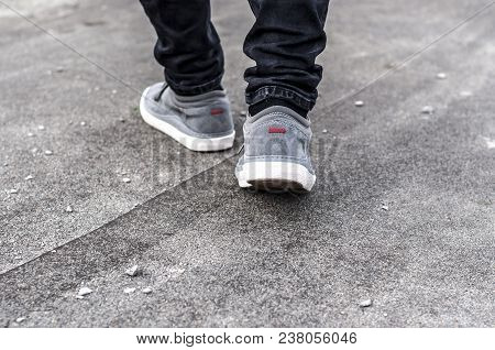 Lower Part Of The Male Legs In Gray Sneakers On The Asphalt Road