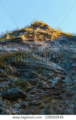 Low-angle View Of A High Steep Rocky Mountain With Cliff Illuminated By The Sun
