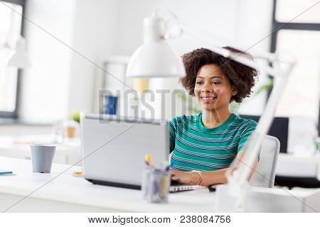 business, education and people concept - happy smiling young african american woman with laptop computer working at office