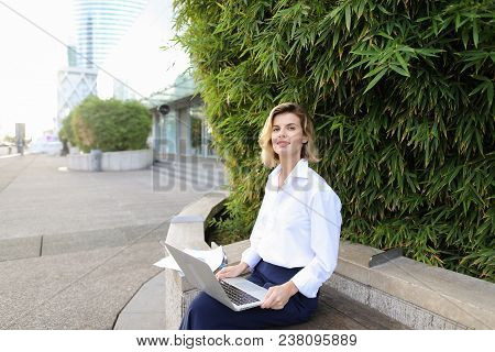 European Businesswoman Working With Laptop And Papers In Open Air Near Green Plant. Concept Of Busin