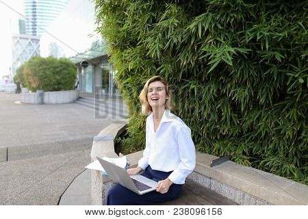 Female Manager Working With Laptop And Papers In Open Air Near Green Plant. Concept Of Busines, Mode
