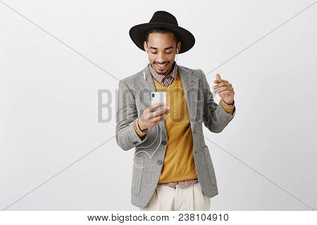 Boosting Happiness With Great Music. Portrait Of Pleased Dancing Dark-skinned Hipster Male In Hat An