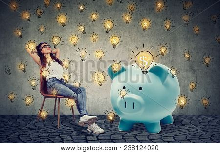 Young Casual Businesswoman With Big Piggy Bank Relaxing Sitting On Chair Generating Bsuiness Ideas