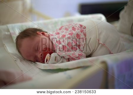 Newborn Baby Sleeping On A Changing Table. Sleeping Baby With Red Pacifier, Closeup.