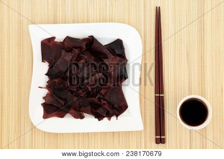 Dulse seaweed super food on a square shaped porcelain dish with low sodium soy sauce and chopsticks on bamboo background. Very high in minerals.