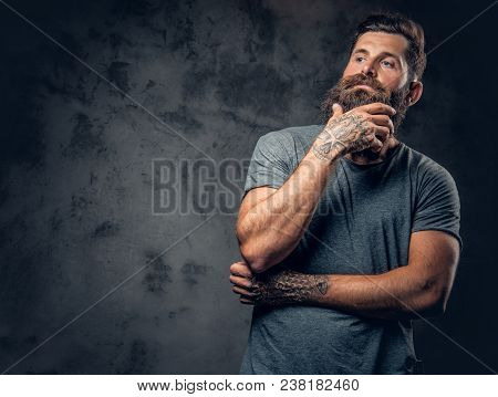 Brutal Bearded Male With Tattooed Arms Over Dark Grey Background.