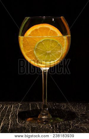 Orange And Lime Slices In A Large Glass On Black Board And Black Background.
