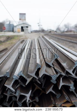 Pile Of New Train Railroad Tracks In Rural Setting, Grain Bins In Background