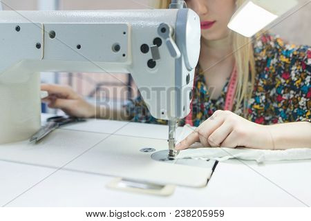 The Seamstress Sits At The Workplace And Sewes On A Sewing Machine. Close-up Work On A Sewing Machin