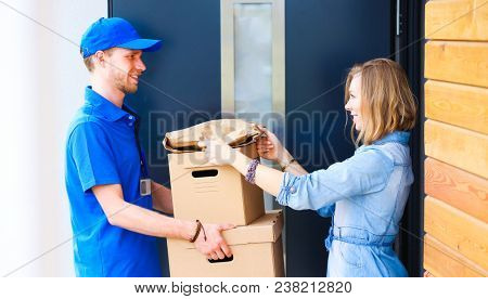 Smiling delivery man in blue uniform delivering parcel box to recipient - courier service concept. Smiling delivery man in blue uniform