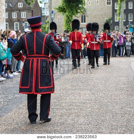 London, UK - 7th June 2017: Rear view of a Beefeater and the Queens Guard on parade at the Tower of London, in traditional red and black uniform with bearskin hats.