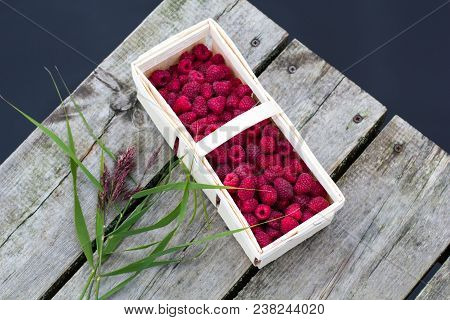 A Small Picnic With A Small Craft Box Of Fresh Organic Raspberries On The Pier At The Lake In The Su