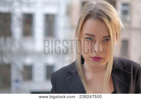 Portrait Of A Young Woman In A Black Suit Close-up Against A Background Of A Blurry City In The Rays