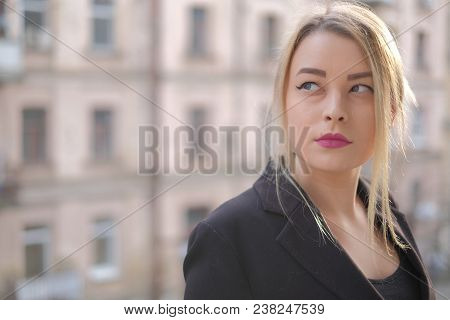 Portrait Of A Young Woman In A Black Suit Close-up Against A Background Of A Blurry City In The Rays